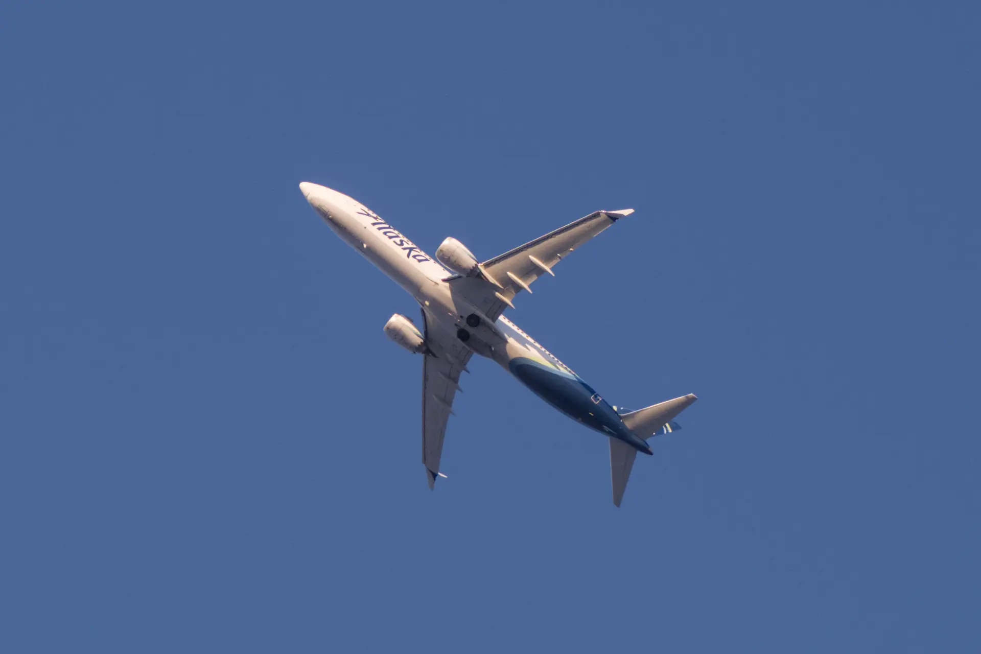 A photo of the underside of an Alaska Airlines twin engine narrowbody passenger liner, climbing away from the camera.