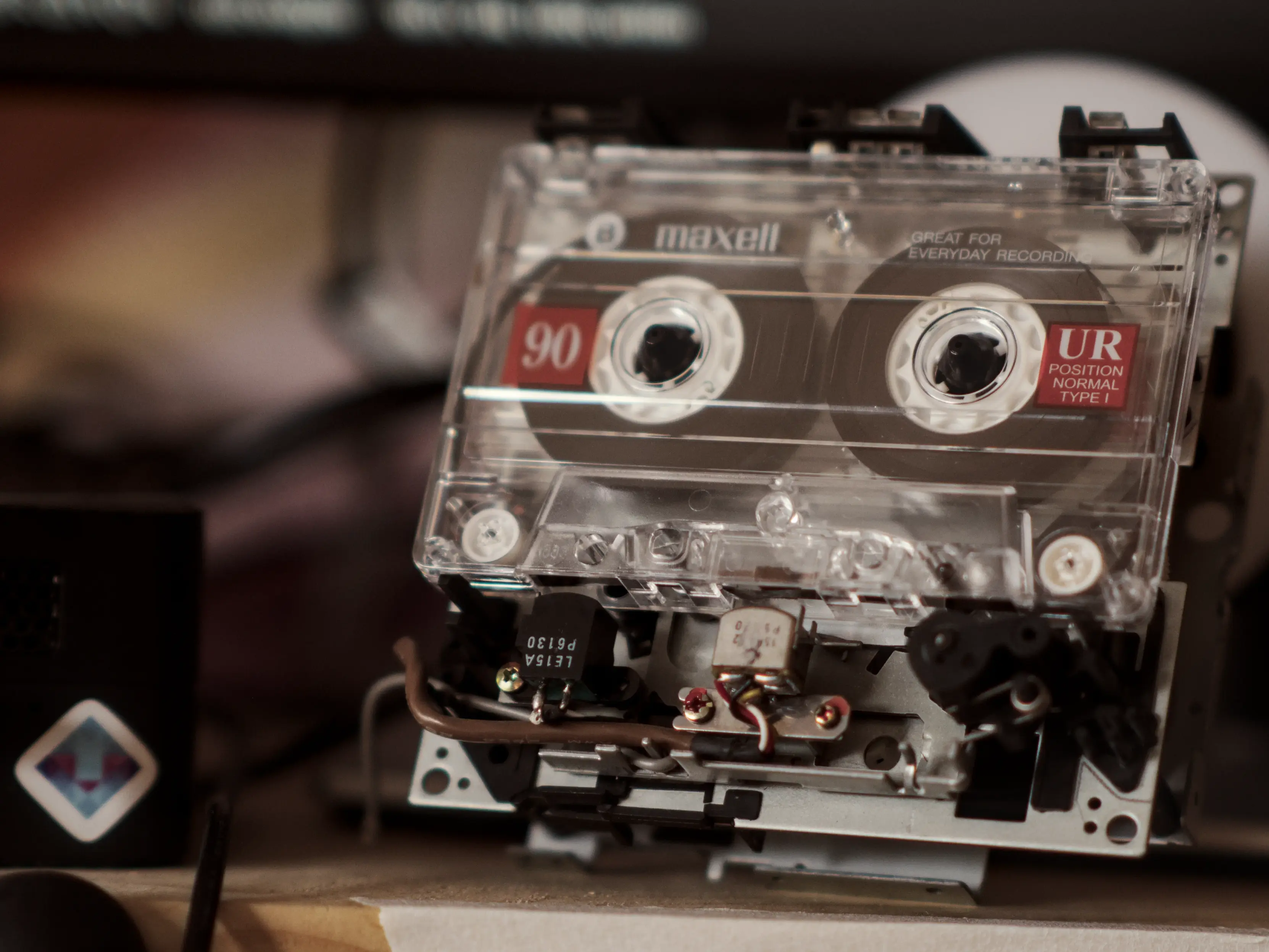 A Maxell tape in a tape mechanism, sitting on a raw wood shelf. The heads and the wires going to them are visible.